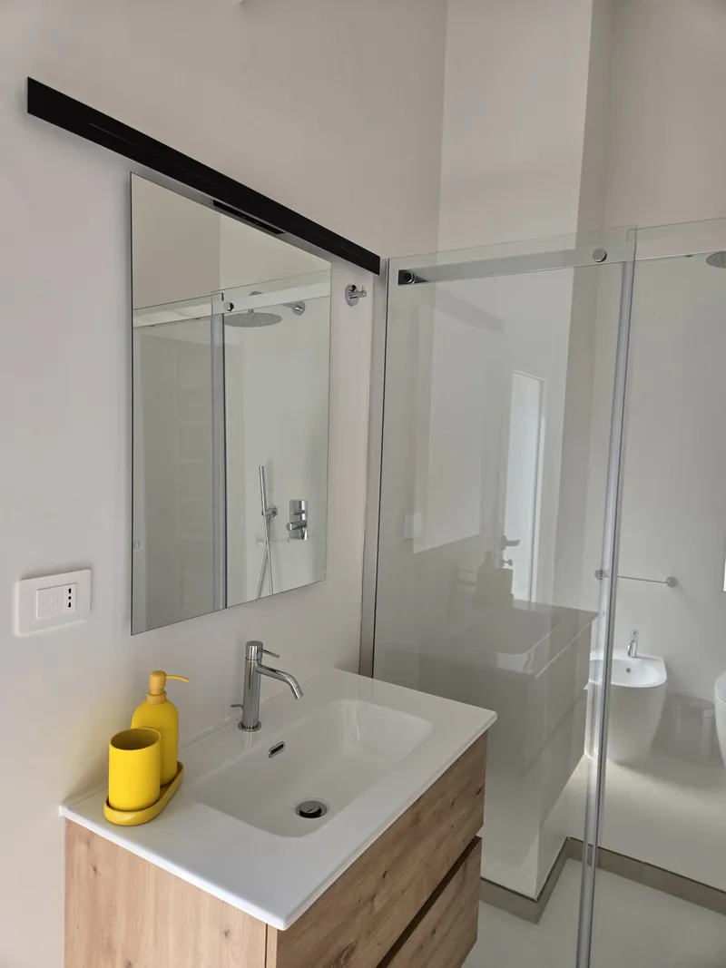 Bagno privato moderno con doccia in vetro e accessori gialli